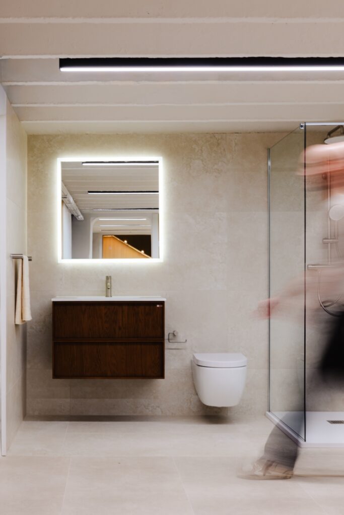 Showroom Fero-Term uređen u soft minimal stilu s kupaonskim ormarićem u boji oraha, pravokutnim ogledalom i mikrocementom na podu.