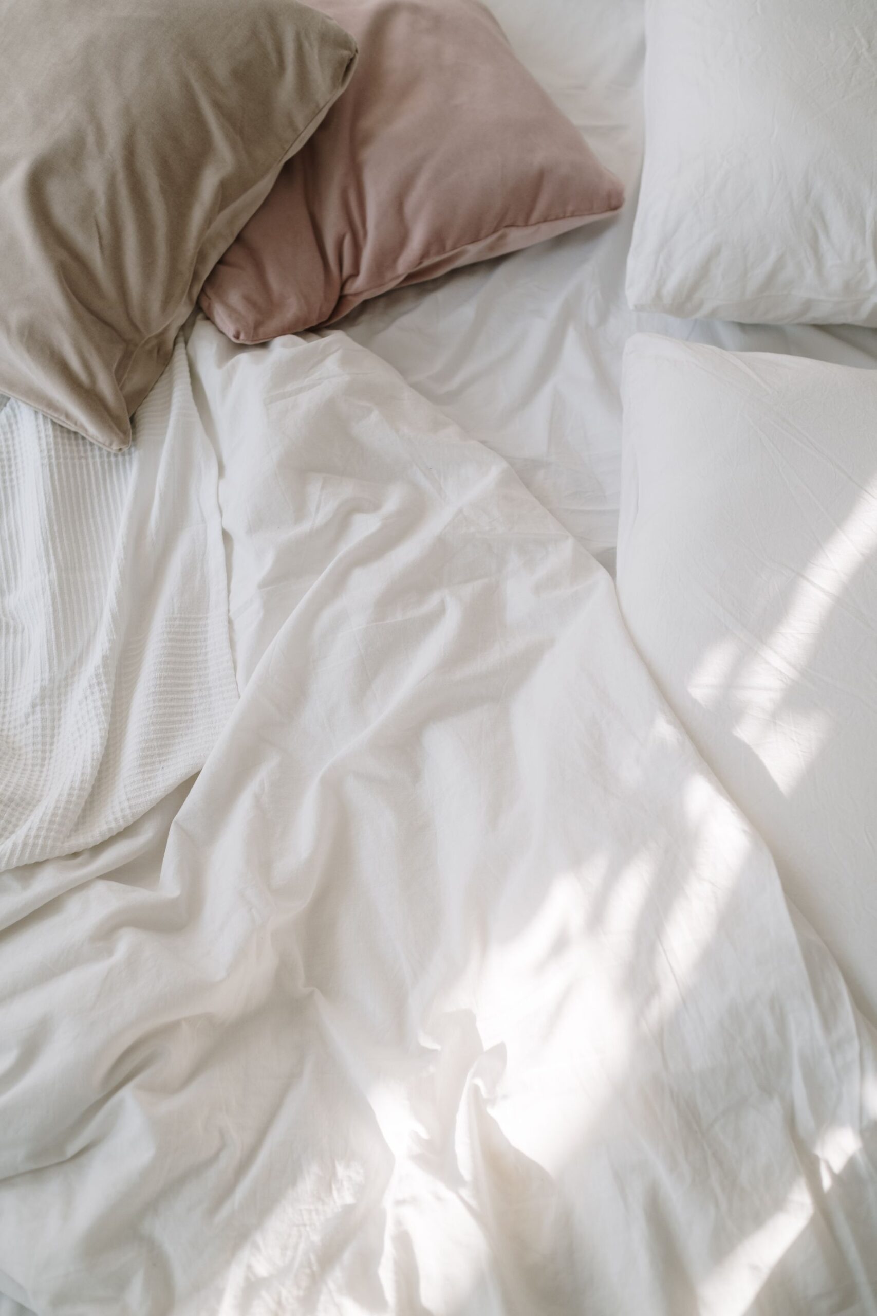 razbarušena posteljina na krevetu slikana odgore s rozim i sivim ukrasnim jastucima te bijelim jastucima 